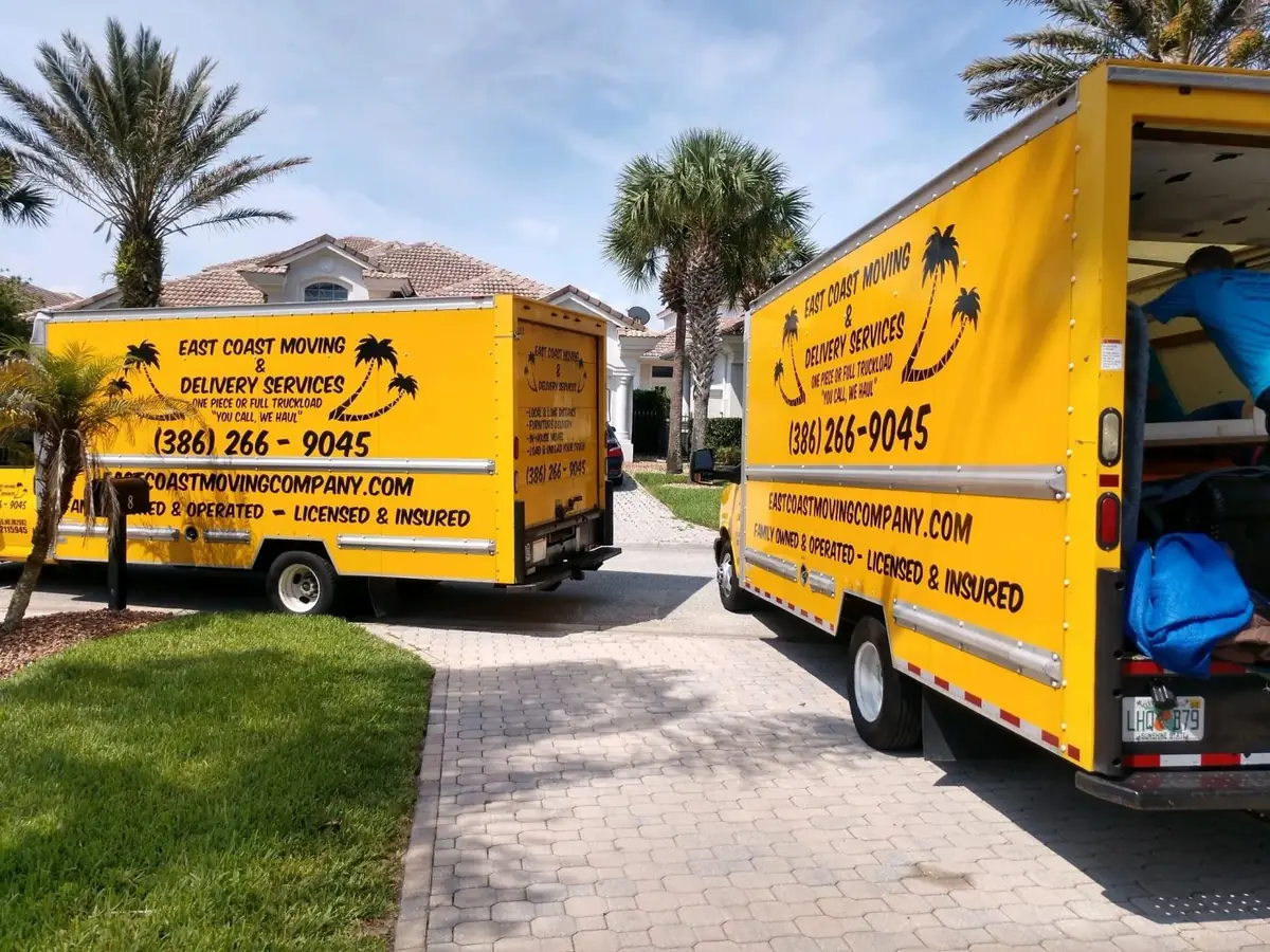 Two East Coast Moving And Delivery Service LLC box trucks parked at a palm-lined home